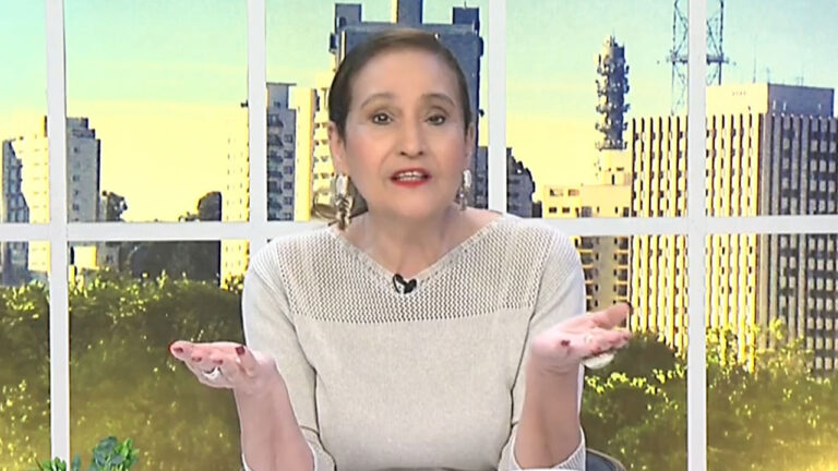 Sonia Abrão com blusa bege de tricot gesticula com as mãos abertas durante a apresentação do programa A Tarde é Sua na RedeTV!