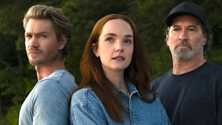 Três pessoas posam lado a lado ao ar livre, com expressão séria e olhar voltado à frente; o homem à esquerda e a mulher ao centro vestem jeans, enquanto o homem à direita usa boné e camiseta escura.