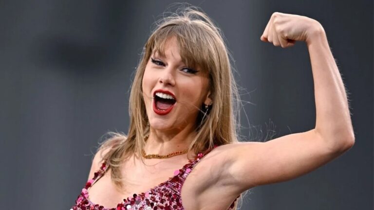 Cantora com vestido vermelho brilhante sorri e levanta o braço em pose durante apresentação musical