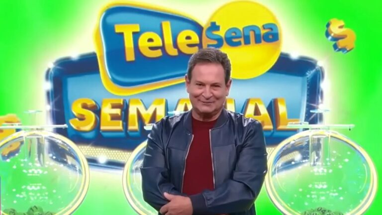 Homem sorri de braços cruzados em estúdio colorido, vestindo jaqueta azul e camisa vermelha, com fundo verde e o logotipo “Tele Sena Semanal” em letras azuis e amarelas atrás dele, ao lado de duas urnas transparentes de sorteio.