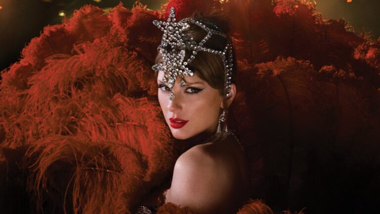 Mulher com batom vermelho e delineado marcado olha para a câmera com expressão intensa, usando adorno brilhante na cabeça em formato de estrela e brincos longos de pedrarias. Ela está cercada por grandes penas vermelhas iluminadas por luz suave, criando um clima de espetáculo e glamour retrô.
