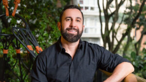 Thiago Garcia sorri de barba e camisa preta em ambiente externo com árvores ao fundo durante entrevista sobre a empresa Xsports