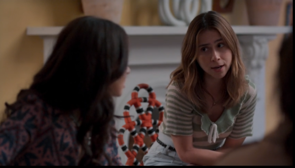 Mulher de blusa listrada verde conversa sentada com outras pessoas em sala decorada com lareira e vasos