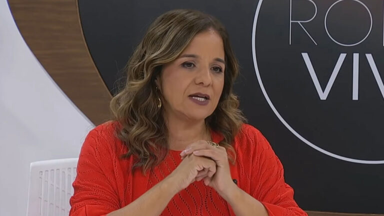 Vera Magalhães de blusa vermelha e mãos entrelaçadas durante apresentação do programa Roda Viva na TV Cultura em São Paulo