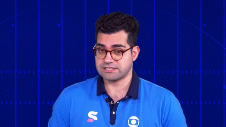 Apresentador de esportes com óculos e camisa azul da Globo fala em estúdio com fundo gráfico durante programa esportivo