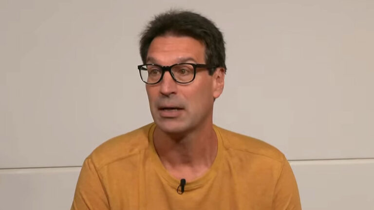 Arnaldo Ribeiro usa camiseta mostarda e óculos durante participação em programa esportivo