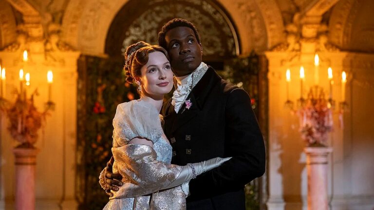Um casal está posando abraçado em um ambiente luxuoso com iluminação quente de velas. A mulher veste um elegante vestido de época claro, com mangas bufantes e luvas longas, e tem o cabelo preso em um penteado clássico. O homem usa traje formal antigo, com casaca escura e gravata branca. Eles olham para cima com expressão serena e confiante. Ao fundo, há uma arquitetura ornamentada com arcos, colunas e arranjos florais, sugerindo um baile ou evento sofisticado ambientado em época histórica.