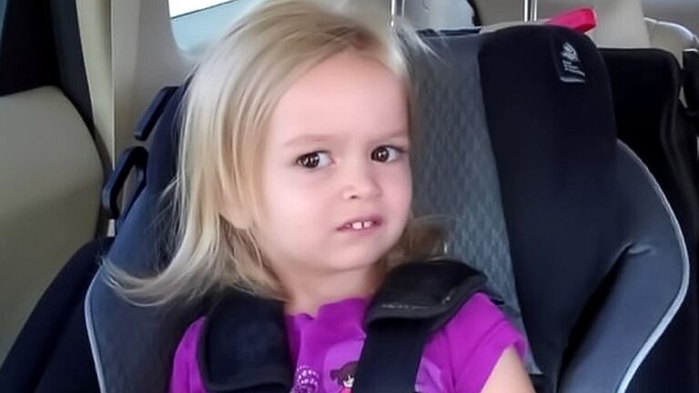Menina loira presa em cadeirinha no banco do carro com expressão de desconfiança em imagem que virou meme nas redes sociais