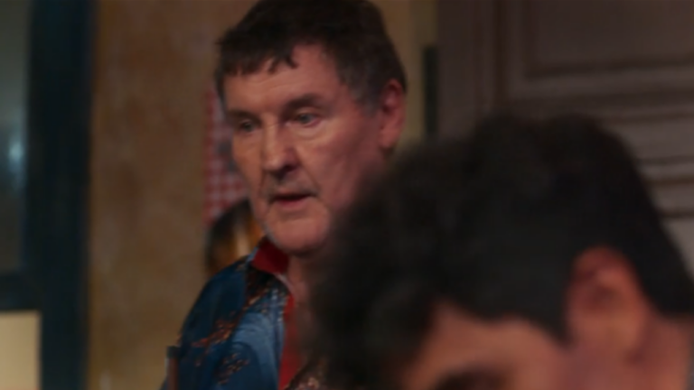 Homem mais velho com expressão séria aparece em ambiente interno durante cena de filme ou série dramática brasileira