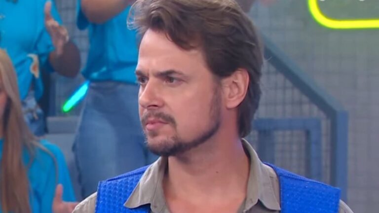 Daniel Erthal em cena de programa de TV com colete azul e expressão séria diante de plateia ao fundo