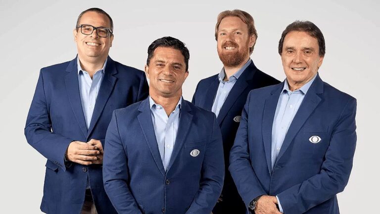 Apresentadores da Band posam de terno azul com logotipo da emissora em foto promocional da Band