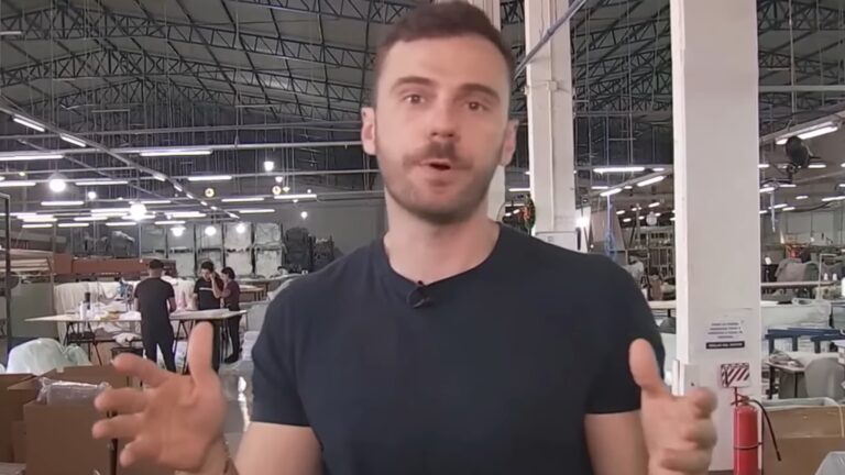 Igor Calian, que é um homem vestindo uma camiseta preta, fala diretamente para a câmera do Documento Band dentro de uma fábrica ou galpão industrial, gesticulando com as mãos; ao fundo, mesas de trabalho, funcionários e estrutura metálica do teto com iluminação fluorescente.