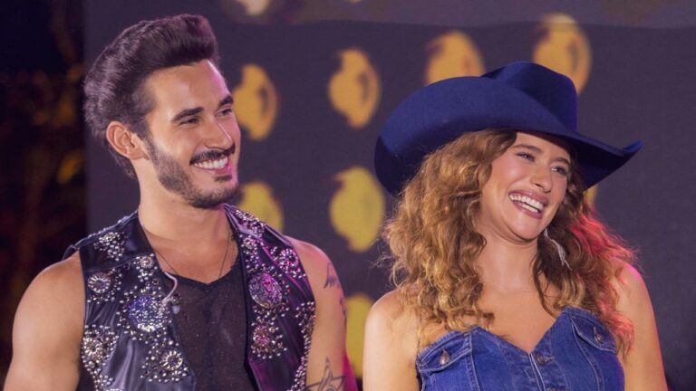 Os atores Filipe Bragança e Isadora Cruz sorriem como os personagens João Raul e Agrado na novela Coração Acelerado, usando roupas em estilo sertanejo