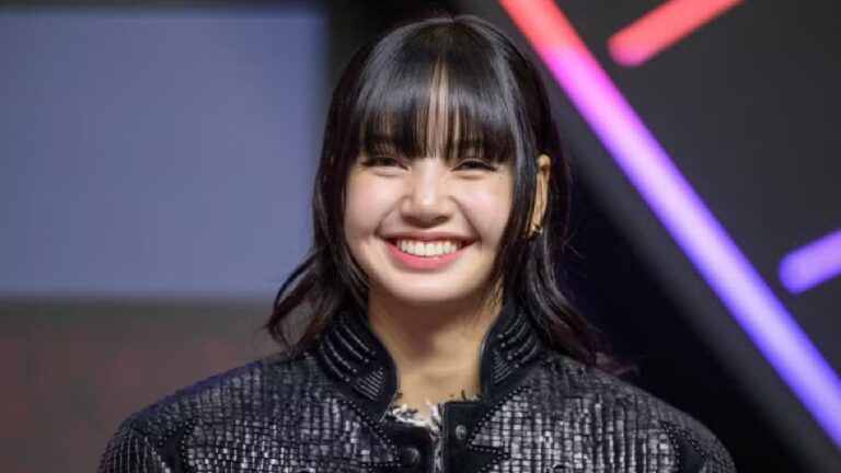 Cantora sorrindo com franja e jaqueta preta durante evento de música com iluminação colorida ao fundo