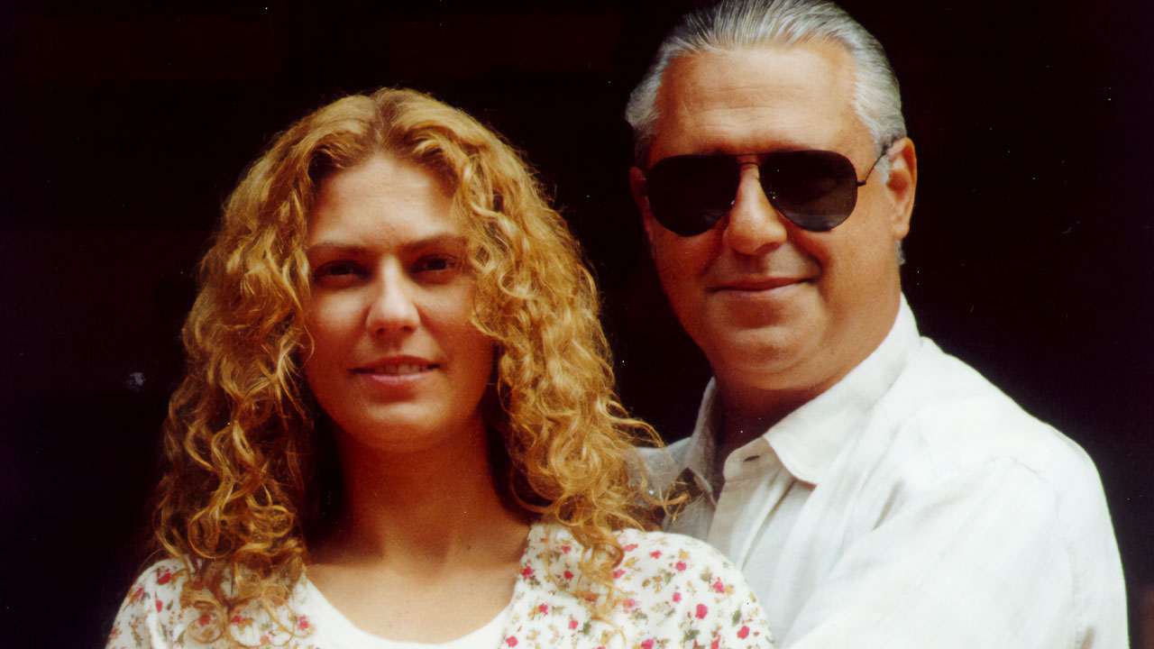 Patrícia Pillar e Antonio Fagundes posam como Luana e Bruno Mezenga na novela O Rei do Gado, ela tem cabelos loiros cacheados e ele usa óculos escuros