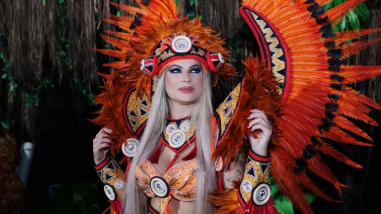 Luciana Fontano posa com fantasia luxuosa de Carnaval em tons de laranja, vermelho e amarelo, com grande cocar de penas e adereços étnicos