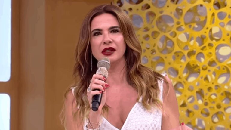 Apresentadora segura microfone e fala em estúdio de programa de TV com cenário amarelo durante atração ao vivo