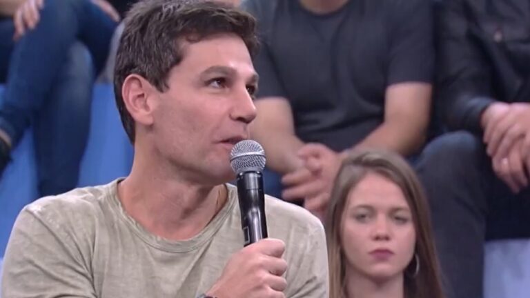 Homem segura microfone e fala para a plateia durante participação em programa de auditório na TV