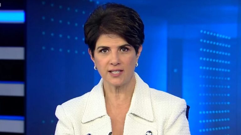 Apresentadora de telejornal com blazer branco fala em estúdio com fundo azul durante edição de noticiário ao vivo