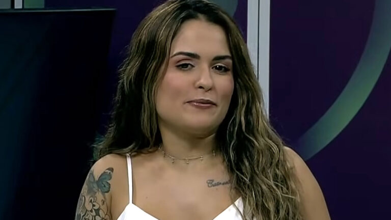 Mariana Rabello ex-apresentadora da TV Serra Dourada afiliada do SBT de blusa branca com tatuagem de borboleta no braço e cabelos longos ondulados em fundo roxo