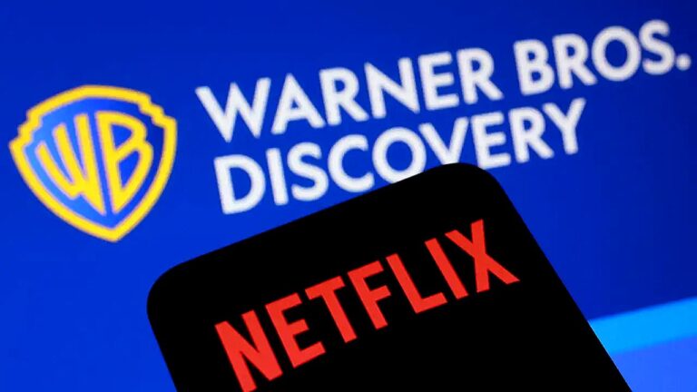 Imagem mostra o logotipo da Warner Bros. Discovery em fundo azul, com o escudo “WB” à esquerda e o texto “WARNER BROS. DISCOVERY” ao lado. Em primeiro plano, aparece parcialmente um celular ou tela com o logotipo da Netflix em vermelho sobre fundo preto, sugerindo relação ou concorrência entre as empresas de entretenimento e streaming.