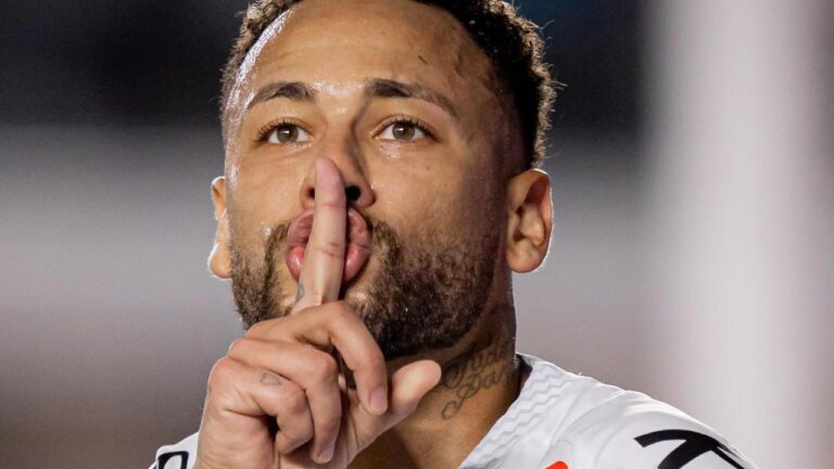 Neymar Jr suado com expressão séria faz sinal de silêncio com o dedo indicador sobre os lábios, veste camisa branca oficial e exibe tatuagens no pescoço