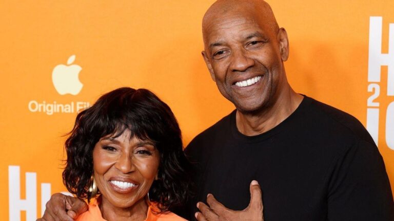 Pauletta Pearson e Denzel Washington sorriem abraçados em um evento, com fundo laranja exibindo a logomarca da Apple Original Films e inscrições brancas