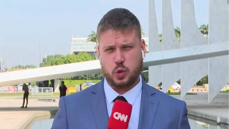 Repórter da CNN com terno azul e microfone vermelho faz entrada ao vivo em frente ao Congresso Nacional em Brasília