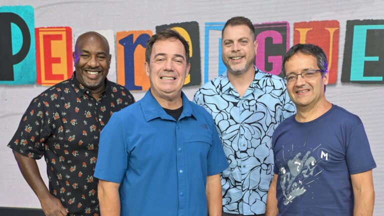 Ângelo Campos, Tatola Godas, Dennys Motta e Ricardo Mendonça posam lado a lado em frente a um painel colorido com a marca do Perrengue na Band. Cada um veste camisa casual diferente — uma estampada escura, uma azul lisa, uma azul com estampa floral e uma camiseta azul com ilustração.
