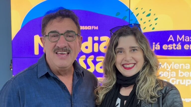 Apresentadores Ratinho e Mylena Ciribelli sorriem lado a lado em frente a um painel digital colorido da Massa FM, em ambiente de rádio bem iluminado