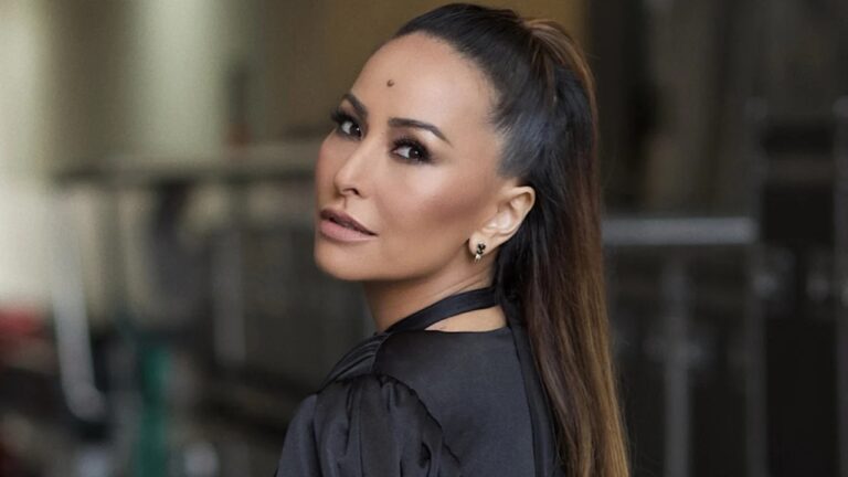 Mulher posa de perfil com cabelo preso em rabo de cavalo e maquiagem marcada em retrato artístico feito em ambiente interno