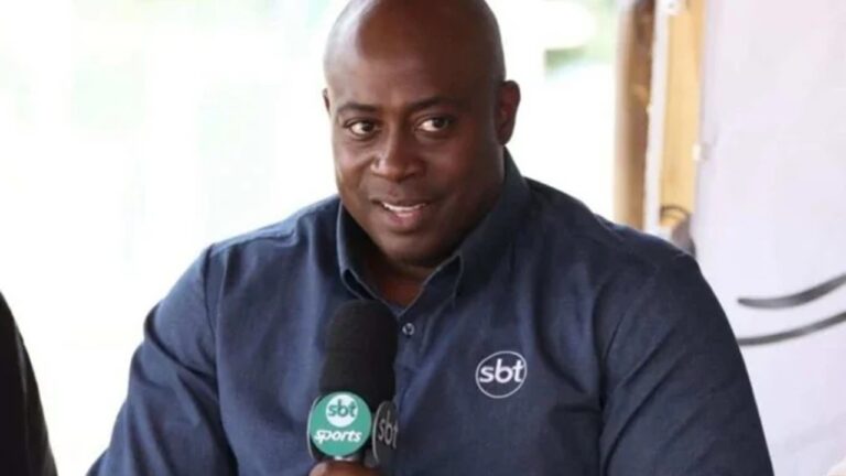 Comentarista esportivo com camisa azul do SBT segura microfone do canal durante transmissão esportiva