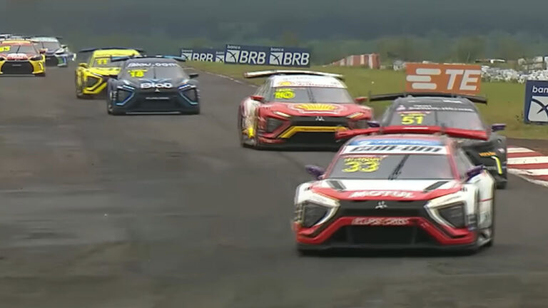 Carros de corrida coloridos da Stock Car em alta velocidade na pista do Autódromo de Campo Grande, com gramado ao fundo e placas publicitárias do BRB