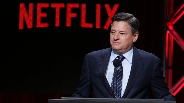 Executivo de terno fala em púlpito durante evento da Netflix com logotipo vermelho da empresa ao fundo