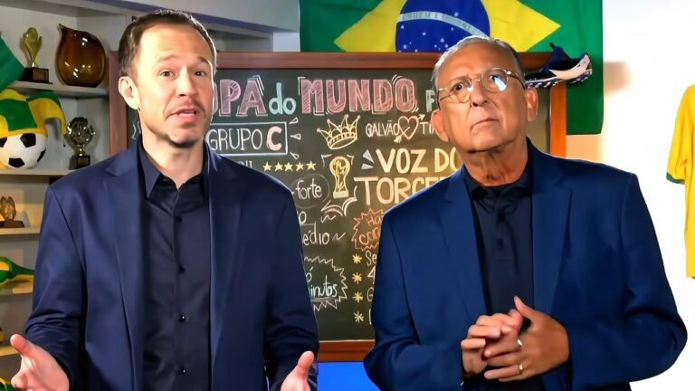 Tiago Leifert e Galvão Bueno vestem paletós azuis em cenário com lousa escrita Copa do Mundo, bandeira do Brasil ao fundo e prateleira com troféus