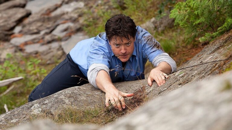 Homem escalando uma grande rocha em um ambiente natural, segurando-se com esforço enquanto olha para cima