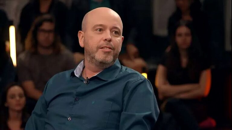 Homem careca fala durante participação em programa de televisão com plateia ao fundo em estúdio iluminado