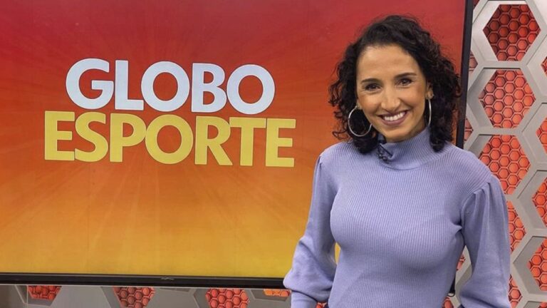 Apresentadora Alice Bastos Neves sorri com cabelos escuros e cacheados, veste blusa de gola alta lilás no cenário do Globo Esporte com fundo laranja