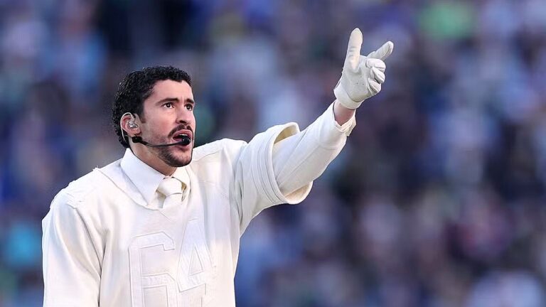 Cantor com roupa branca e luvas aponta para o público durante apresentação em estádio com microfone headset