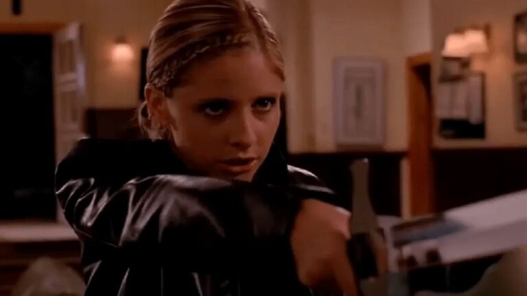 Mulher loira com expressão intensa segura estaca de madeira em cena de ação sobrenatural em ambiente interno