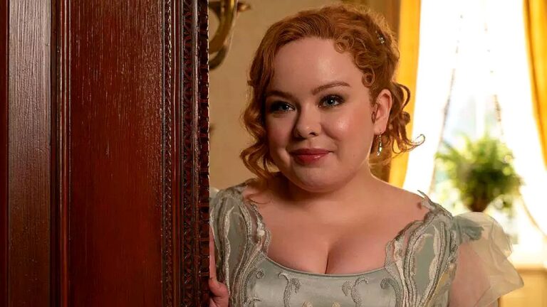 Mulher ruiva com vestido de época aparece sorrindo discretamente ao lado de porta em ambiente interno iluminado com decoração clássica