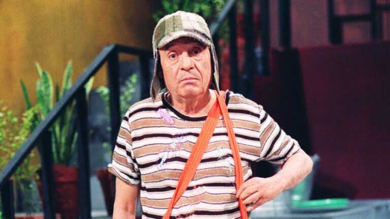 Roberto Gómez Bolaños caracterizado como Chaves na vila, ele usa boné xadrez de abas laterais e camiseta listrada com suspensório laranja no ombro