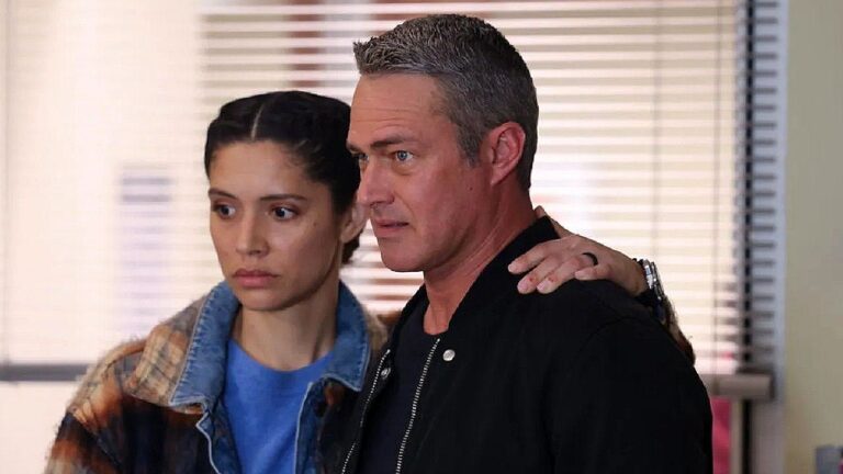 Mulher apoia a mão no ombro de homem com expressão tensa em cena de série dentro de escritório