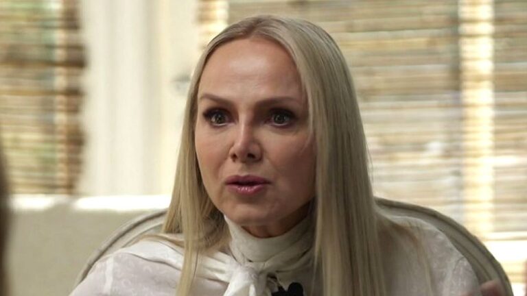 Mulher loira com expressão séria durante entrevista em programa de televisão em ambiente interno iluminado