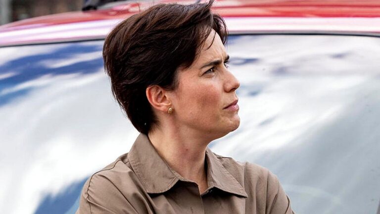 Mulher de cabelo curto observa ao lado de carro com expressão séria em cena externa