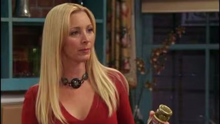 Mulher loira segura pote e conversa em cena de série ambientada em cozinha