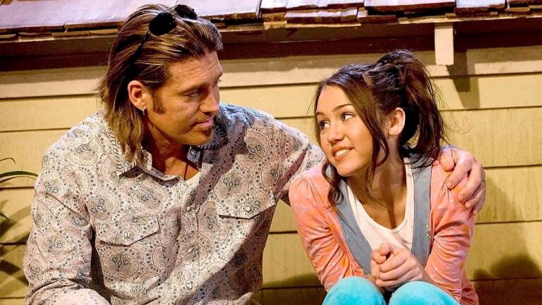 Texto Alternativo disse: Homem abraça jovem enquanto conversam sentados em escada em cena de filme com clima familiar