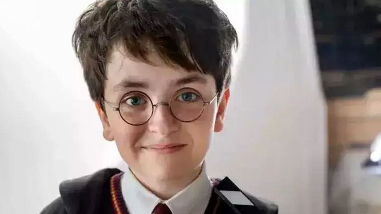 Menino com óculos redondos e uniforme escolar inspirado em Harry Potter olha para câmera em cena de filme