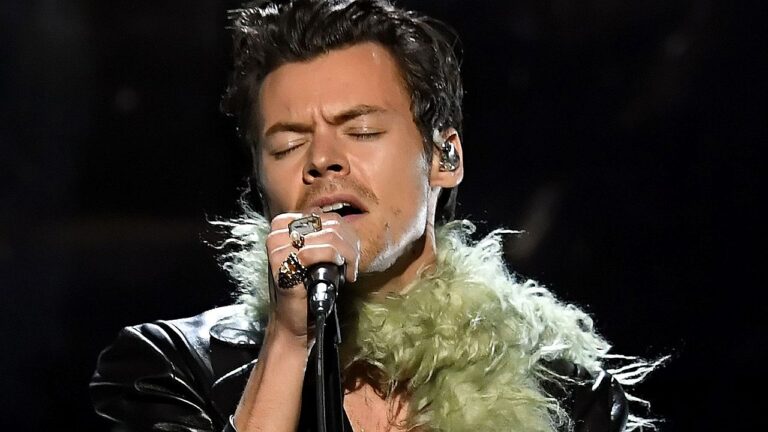 Cantor segura microfone e canta com olhos fechados durante apresentação em palco com iluminação escura ao fundo