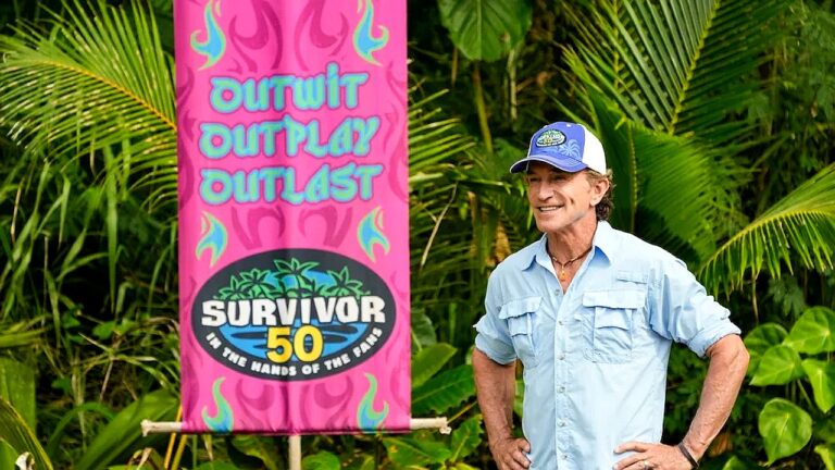 Apresentador de Survivor posa ao lado de painel com slogan Outwit Outplay Outlast em cenário de selva tropical